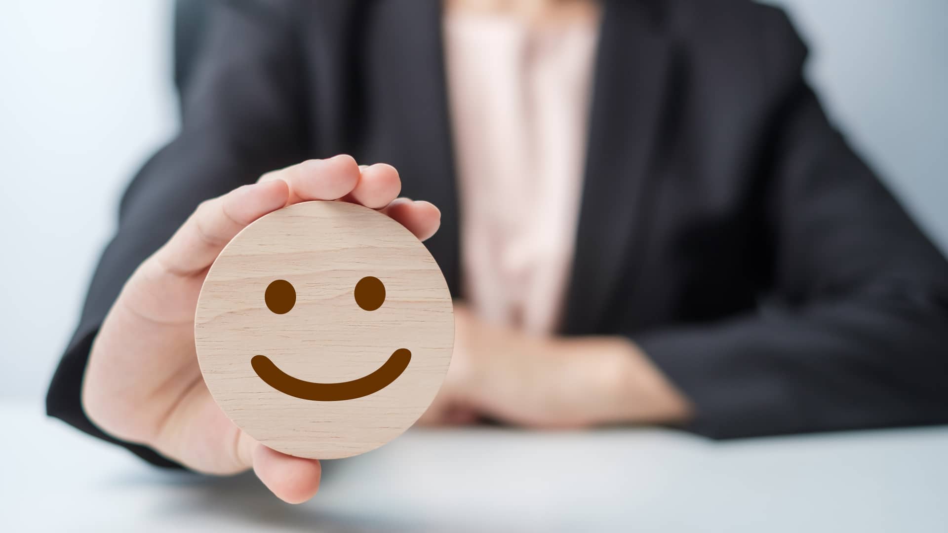 Una mujer sostiene un círculo de madera con una carita sonriente representando las opiniones de los clientes de iris energía