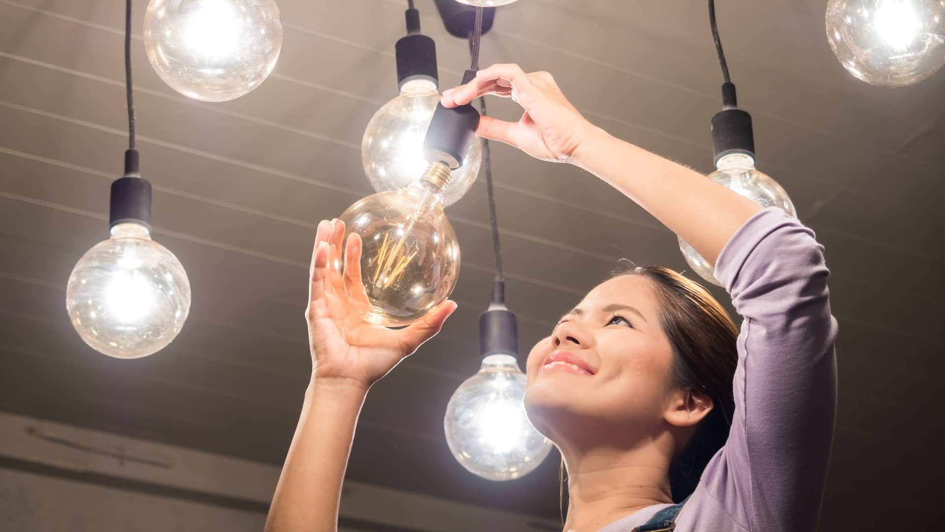 Mujer cambiando una de las bombillas de su local que se beneficia de una de las tarifas de luz de la compañía Plenitude