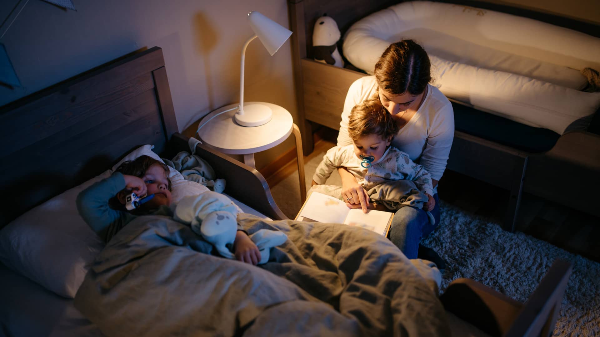 Madre leyendo un libro a sus dos hijos bajo la luz de un flexo