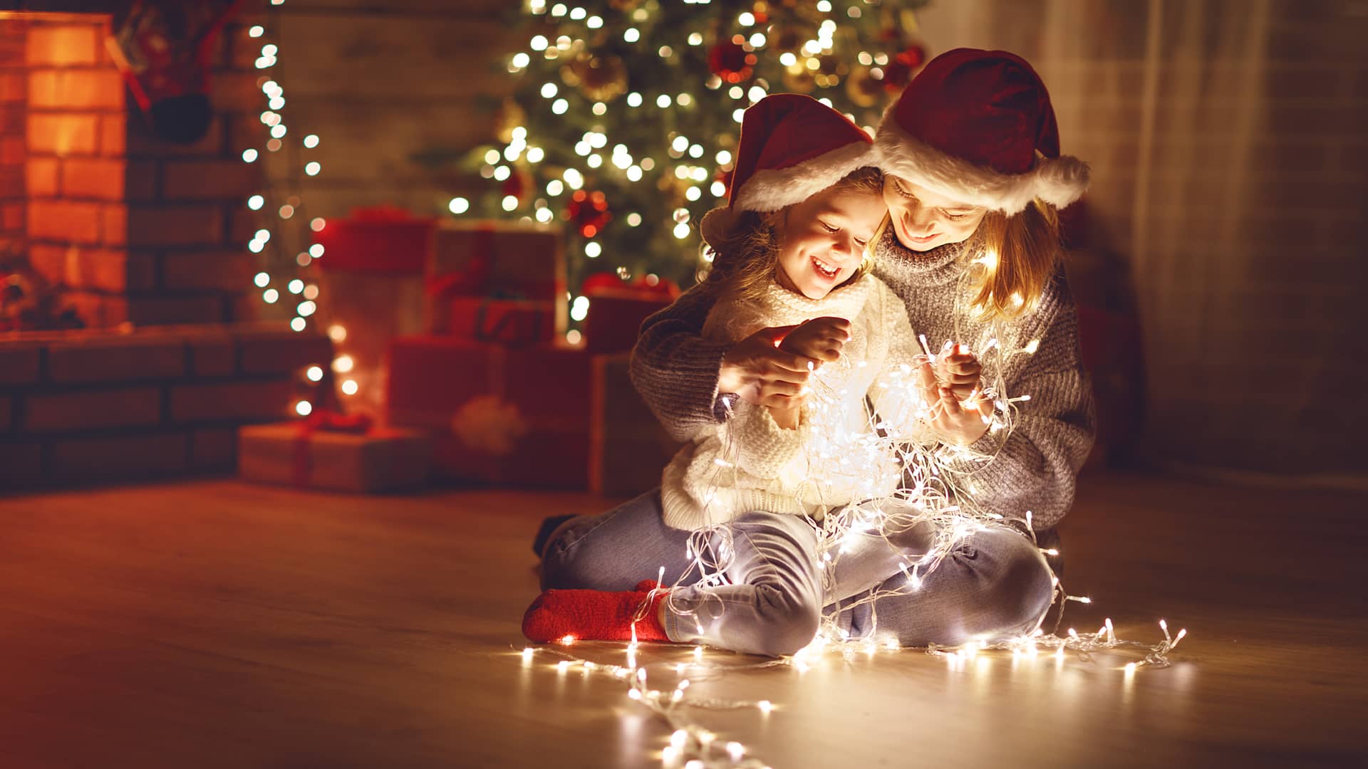 Madre e hija jugando con guirnalda con luces navideña cerca del arbol de navidad