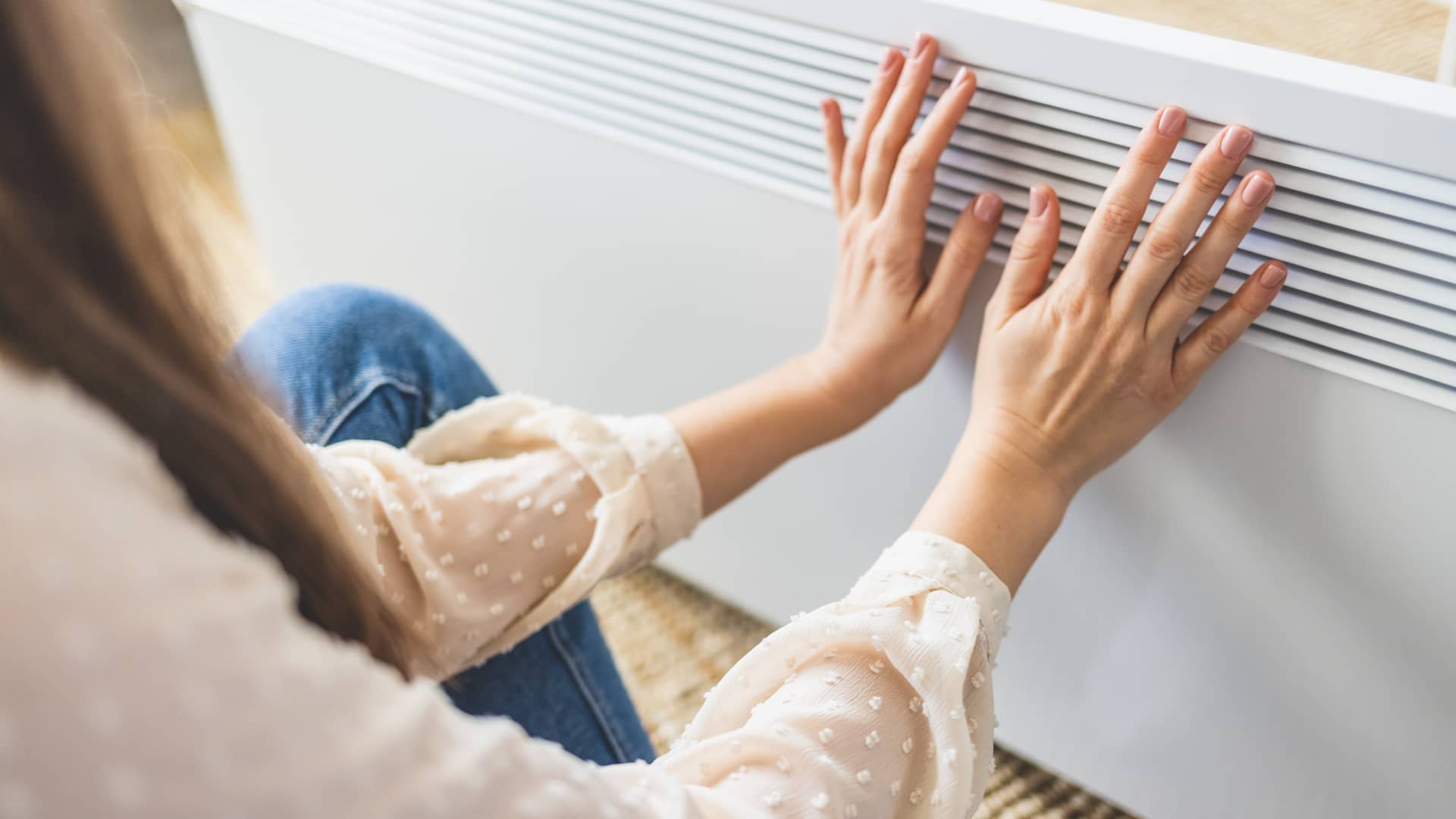 Mujer calentandose en un radiador eléctrico, te ayudamos a realizar la elección entre calefacción eléctrica o de gas 